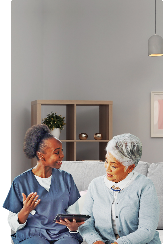 Female caregiver holding a tablet while talking to the elder woman