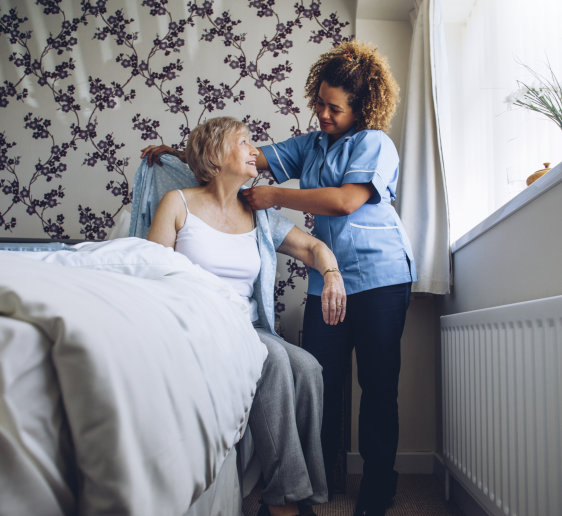 Curly female caregiver put a clothes to the elder woman