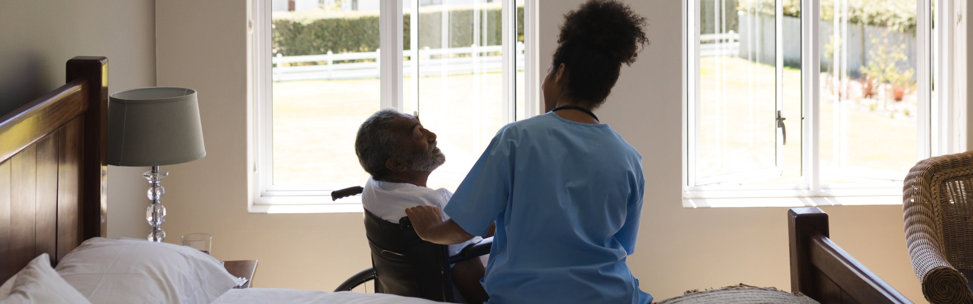 Elder man sitting on a wheelchair at his room with his caregiver